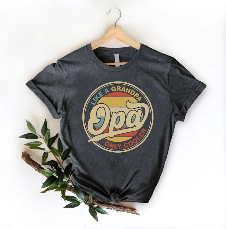 May include: A dark grey t-shirt with a vintage-style circular graphic that says "Like a Grandpa, Only Cooler" with the word "Opa" in a larger font.