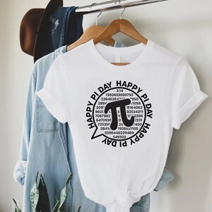 Puede incluir: Camiseta blanca con un gr&aacute;fico negro de un globo de di&aacute;logo con el texto "Happy Pi Day" y un gran s&iacute;mbolo pi rodeado de n&uacute;meros.