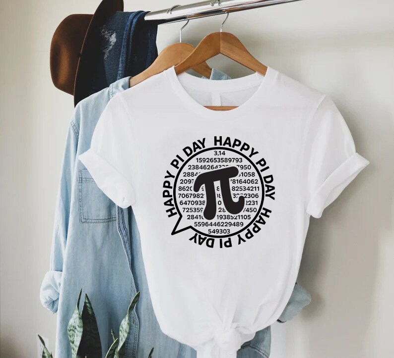 Puede incluir: Camiseta blanca con un gr&aacute;fico negro de un globo de di&aacute;logo con el texto "Happy Pi Day" y un gran s&iacute;mbolo pi rodeado de n&uacute;meros.