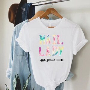 May include: White t-shirt with a tie-dye effect design that says "Mail Lady" with the name "Jessica" written below it.