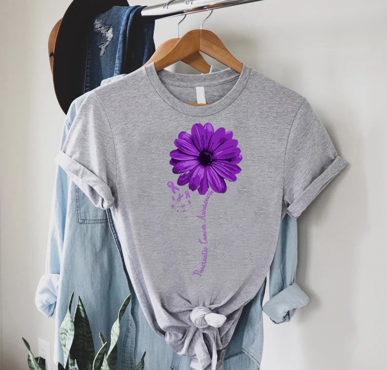 K&ouml;nnte beinhalten: Ein graues T-Shirt mit einer lila Blume und dem Text "Pancreatic Cancer Awareness" auf der Vorderseite.