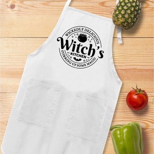 May include: White kitchen apron with a black circle design that says "Wickedly Delicious Witch's Kitchen Stirring Up Some Magic" with a cauldron and bats.