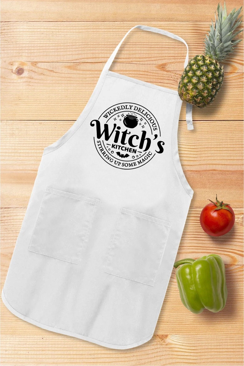 May include: White kitchen apron with a black circle design that says "Wickedly Delicious Witch's Kitchen Stirring Up Some Magic" with a cauldron and bats.