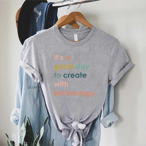 May include: A grey t-shirt with the text "it's a good day to create with technology." The text is in different colours, including orange, yellow, green, and blue.