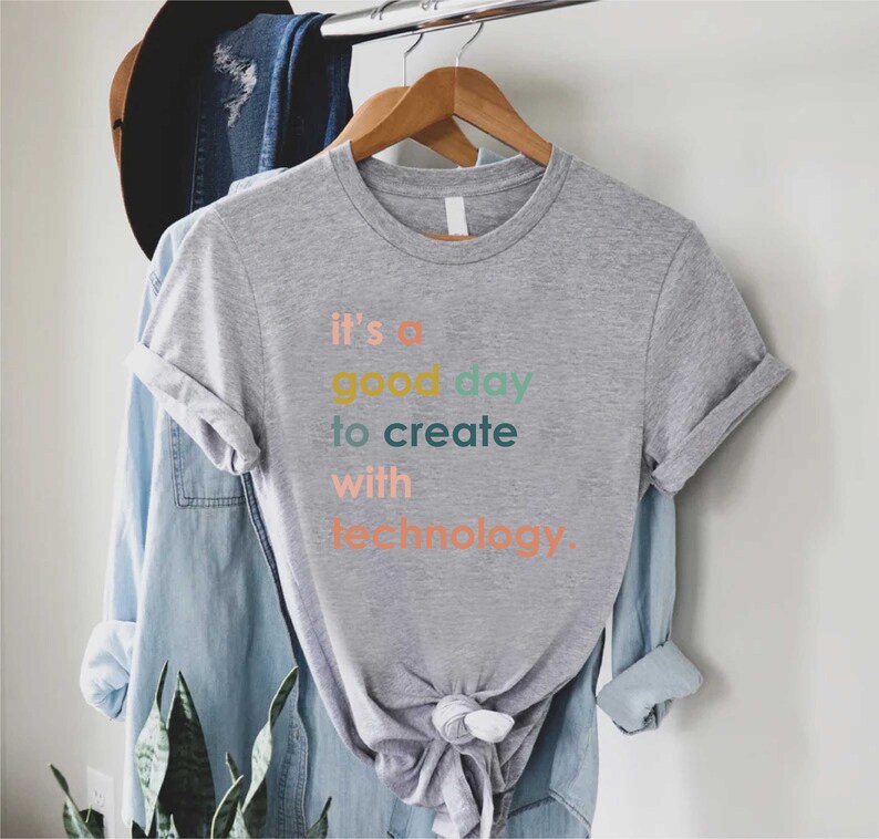 May include: A grey t-shirt with the text "it's a good day to create with technology." The text is in different colours, including orange, yellow, green, and blue.