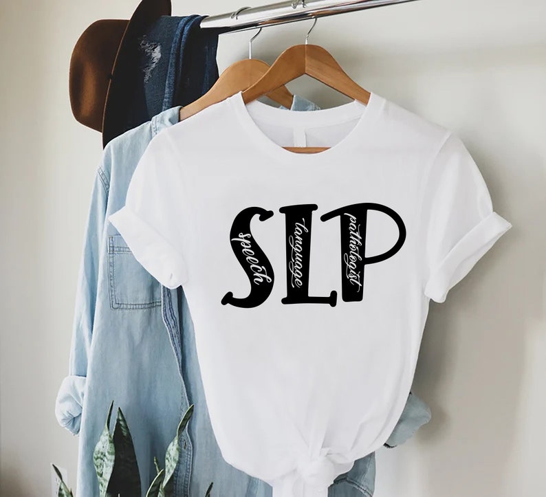 Puede incluir: Camiseta blanca con las letras "SLP" en negro, con las palabras "speech", "language" y "pathologist" escritas verticalmente dentro de las letras.