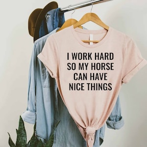 Może przedstawiać: R&oacute;żowy T-shirt z nadrukiem "Pracuję ciężko, żeby m&oacute;j koń miał fajne rzeczy" w kolorze czarnym.
