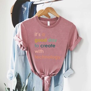 May include: A pink t-shirt with the text "it's a good day to create with technology" in colourful letters.