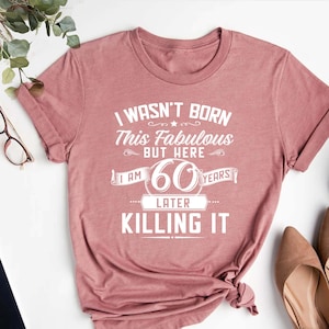 May include: A pink t-shirt with the text "I wasn't born this fabulous but here I am 60 years later killing it".