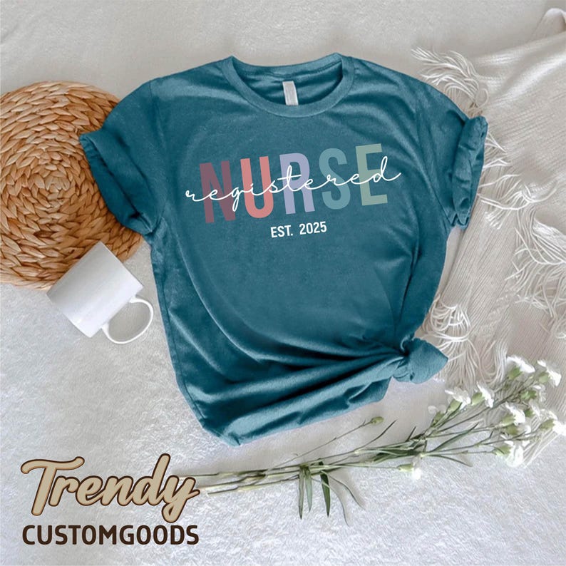 K&ouml;nnte beinhalten: Tealblaues T-Shirt mit dem Text "NURSE registered EST. 2025" in Regenbogenfarben.
