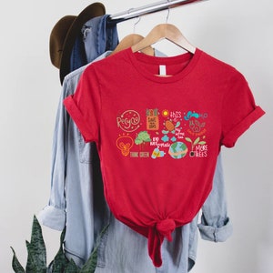Puede incluir: Camiseta roja con un dise&ntilde;o gr&aacute;fico que presenta una bombilla, &aacute;rboles, un globo terr&aacute;queo y las palabras "Recicla", "Salva nuestros mares", "Piensa en verde", "Este tambi&eacute;n es mi hogar", "No uses pl&aacute;stico", "H2O Ahorra energ&iacute;a" y "M&aacute;s &aacute;rboles".