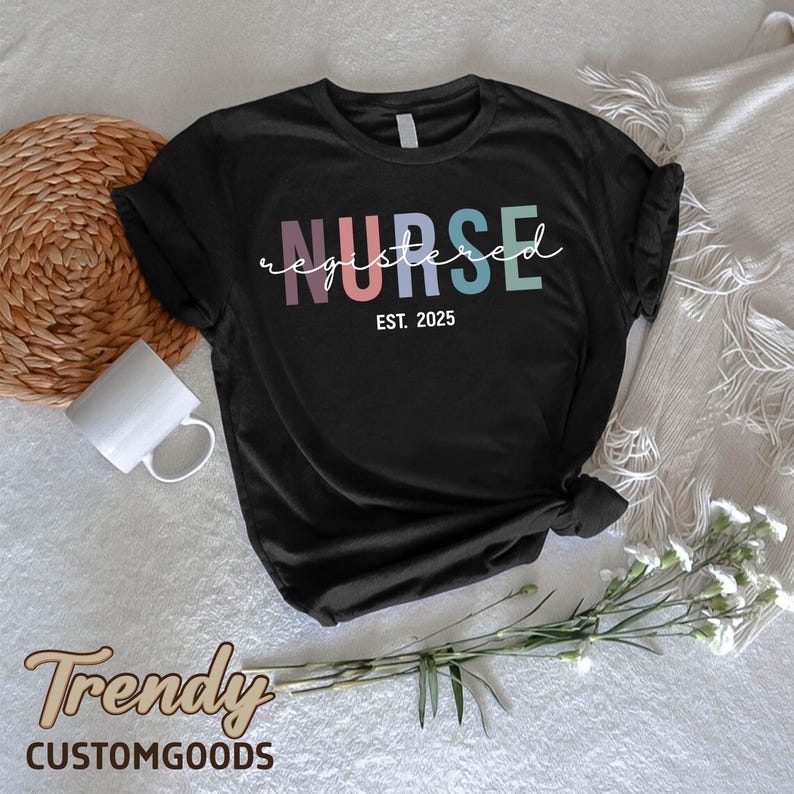 K&ouml;nnte beinhalten: Schwarzes T-Shirt mit dem Text "NURSE registered EST. 2025" in Regenbogenfarben. Der Text ist in einer kursivschrift.