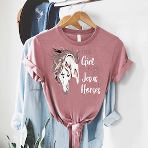 May include: A pink t-shirt with a graphic of a horse's head and the text "This Girl Runs On Jesus And Horses".