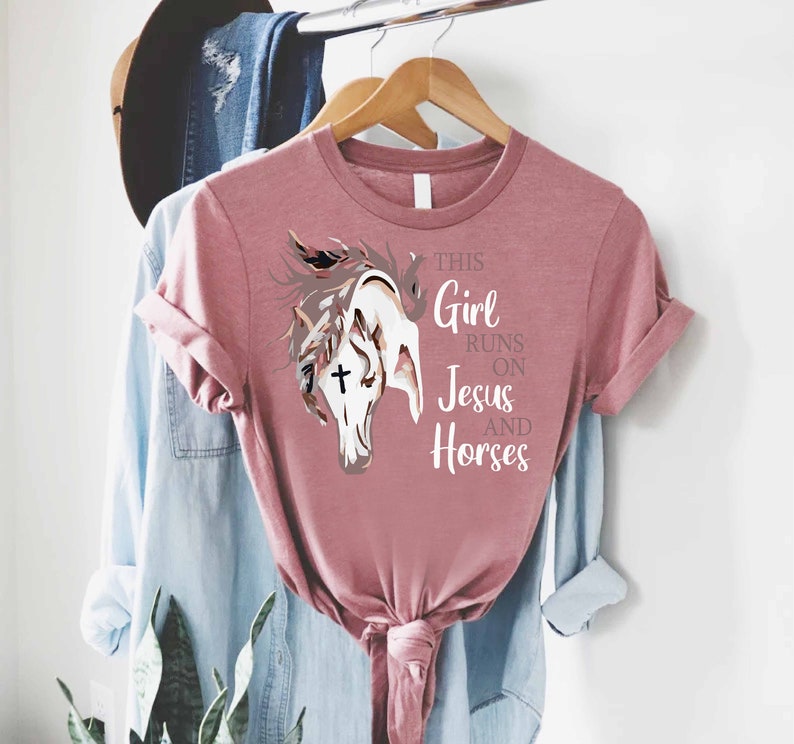 May include: A pink t-shirt with a graphic of a horse's head and the text "This Girl Runs On Jesus And Horses".