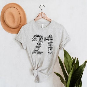 May include: Gray t-shirt with a black number "21" made of words related to birthdays and celebrations, such as "Happy", "Birthday", "Gifts", "Friends", and "Wish".