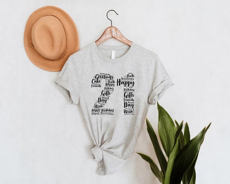 May include: Gray t-shirt with a black number "21" made of words related to birthdays and celebrations, such as "Happy", "Birthday", "Gifts", "Friends", and "Wish".