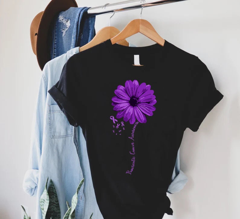 K&ouml;nnte beinhalten: Schwarzes T-Shirt mit einer lila Blume und dem Text "Pancreatic Cancer Awareness".