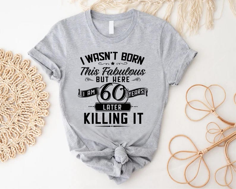 May include: Gray t-shirt with black text that reads "I wasn't born this fabulous but here I am 60 years later killing it".