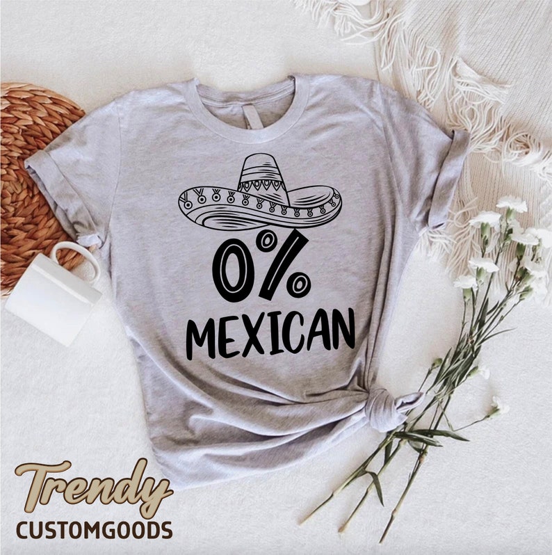 Op de afbeelding: Een grijs T-shirt met een zwart-witte illustratie van een sombrero en de tekst "0% Mexicaans".