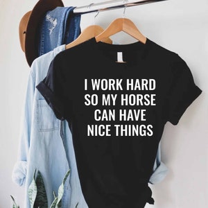 Może przedstawiać: Czarny T-shirt z białym napisem: "Pracuję ciężko, żeby m&oacute;j koń miał fajne rzeczy".