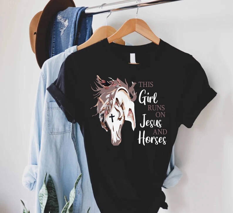 May include: Black t-shirt with a white horse illustration and the text "This Girl Runs On Jesus And Horses".
