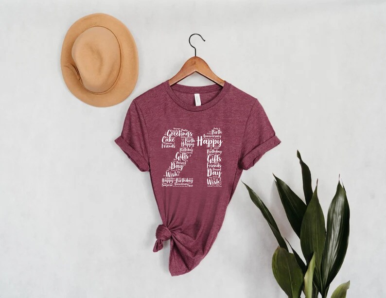 May include: A maroon t-shirt with a white graphic design of the number 22 made up of words related to birthdays, such as "Happy", "Birthday", "Cake", "Friends", and "Gifts".