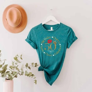May include: Teal t-shirt with a gold glitter circle design that says "50th Birthday Queen Sassy, Classy, Fabulous". The number 50 is gold glitter and there is a red lip and a gold crown in the circle.