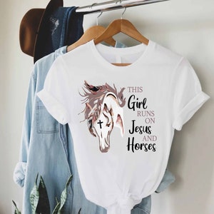 May include: White t-shirt with a brown and white horse illustration and the text "This Girl Runs On Jesus And Horses".