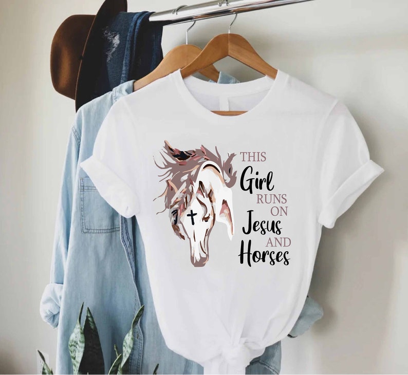May include: White t-shirt with a brown and white horse illustration and the text "This Girl Runs On Jesus And Horses".