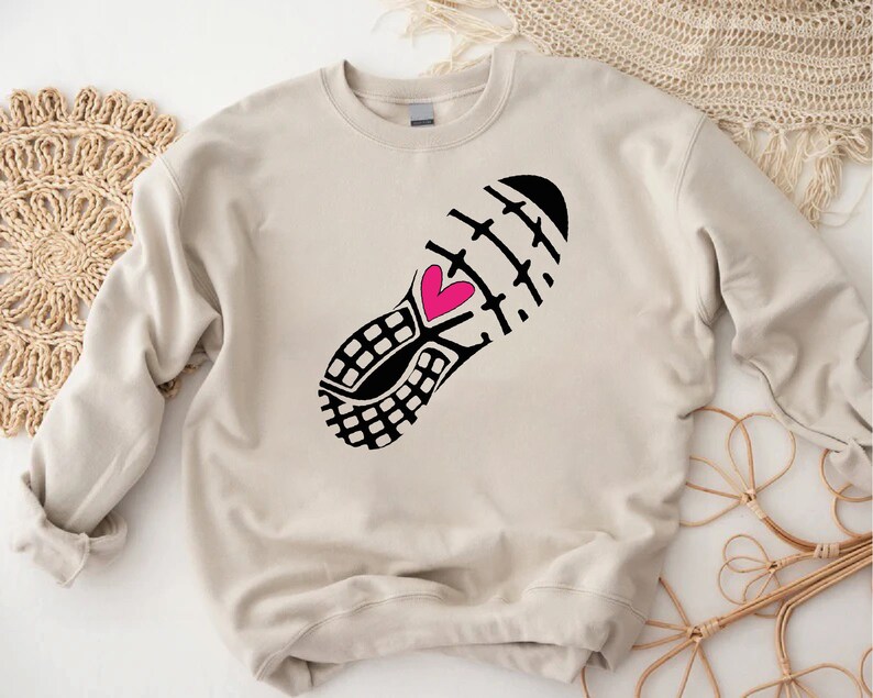 Peut inclure: Un sweat-shirt beige avec un imprim&eacute; noir et blanc d'une chaussure de course avec un c&oelig;ur rose.