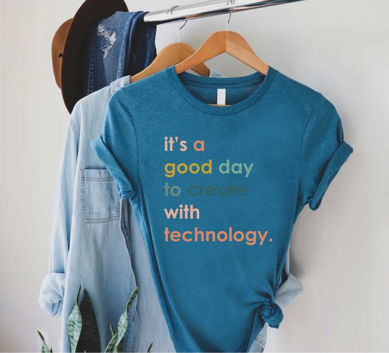 May include: A teal blue t-shirt with the text "it's a good day to create with technology." in colourful letters.
