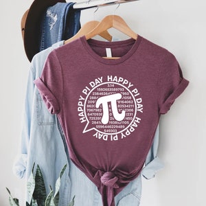 Puede incluir: Una camiseta color granate con un gr&aacute;fico blanco que dice "Happy Pi Day" con un c&iacute;rculo alrededor del texto que incluye el s&iacute;mbolo matem&aacute;tico de pi y los primeros 30 d&iacute;gitos de pi.