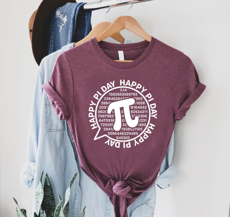Puede incluir: Una camiseta color granate con un gr&aacute;fico blanco que dice "Happy Pi Day" con un c&iacute;rculo alrededor del texto que incluye el s&iacute;mbolo matem&aacute;tico de pi y los primeros 30 d&iacute;gitos de pi.