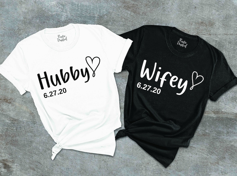 May include: Two white t-shirts with black text. One shirt says "Hubby" with a heart and the date "6.27.20". The other shirt says "Wifey" with a heart and the date "6.27.20".