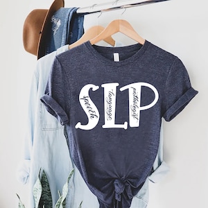 Puede incluir: Una camiseta azul marino con texto blanco que dice "SLP" con las palabras "speech", "language" y "pathologist" escritas verticalmente dentro de las letras.