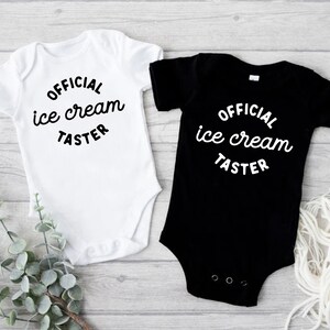 Puede incluir: Dos bodies para beb&eacute;, uno blanco y otro negro, con el texto "OFFICIAL ice cream TASTER" en una fuente cursiva blanca.