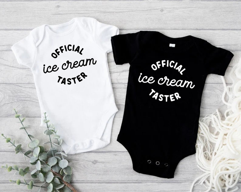 Puede incluir: Dos bodies para beb&eacute;, uno blanco y otro negro, con el texto "OFFICIAL ice cream TASTER" en una fuente cursiva blanca.