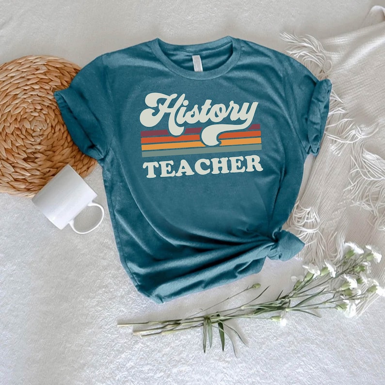 May include: Teal blue t-shirt with the text "History Teacher" in a retro font with a rainbow stripe design.