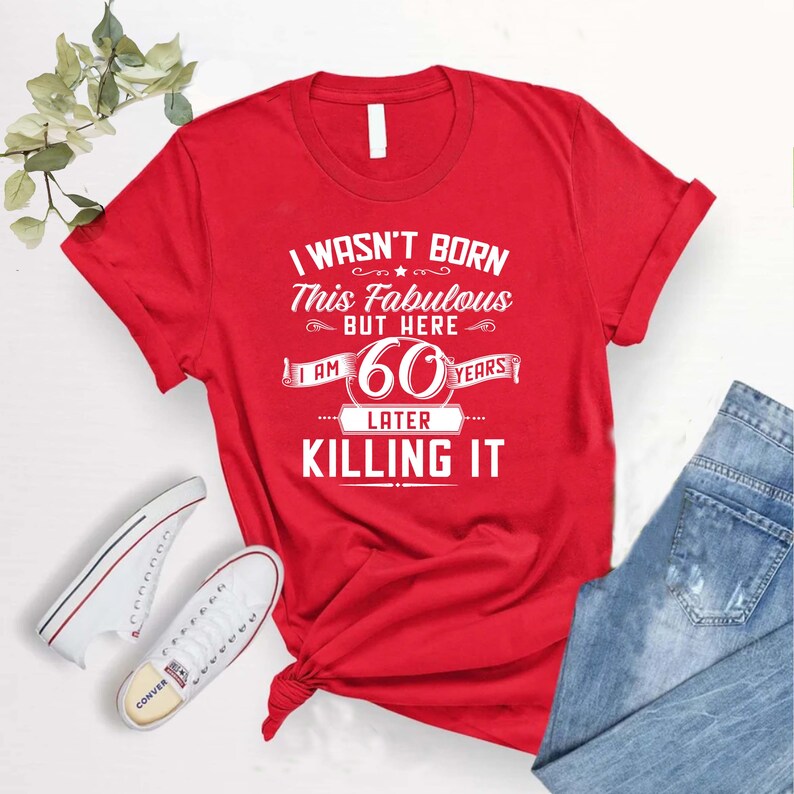 May include: Red t-shirt with white text that reads "I wasn't born this fabulous but here I am 60 years later killing it".