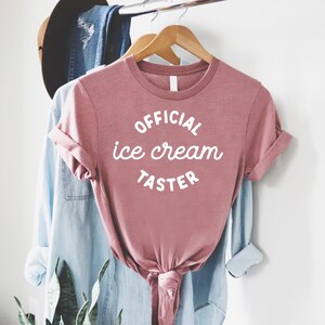 Puede incluir: Una camiseta rosa con el texto "OFFICIAL ice cream TASTER" en blanco.