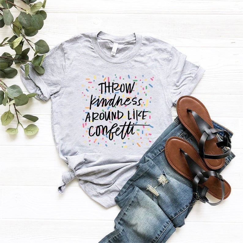 Może przedstawiać: Szara koszulka z nadrukiem "Throw kindness around like confetti" w czarnym kolorze pisma z kolorowymi konfetti otaczającymi tekst.