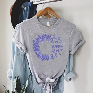 May include: A grey t-shirt with a purple sunflower design. The sunflower is made up of purple ribbons and butterflies.