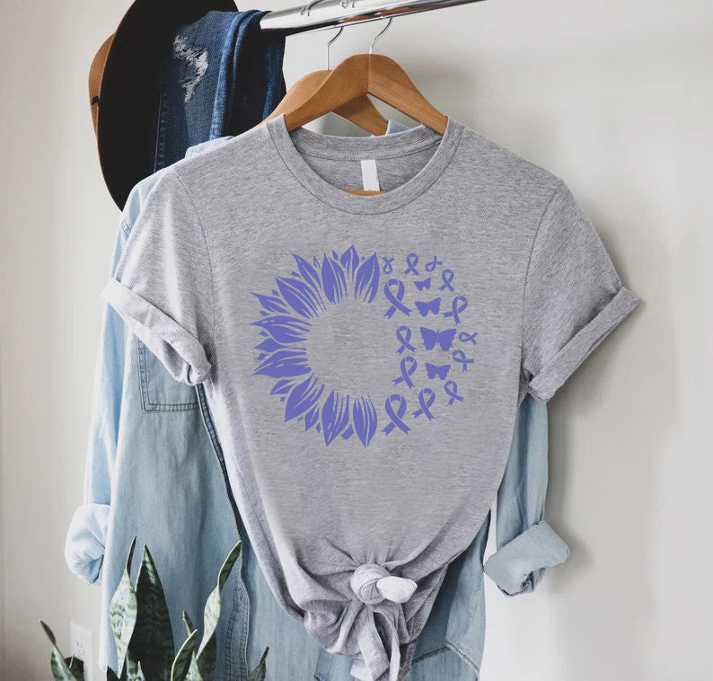 May include: A grey t-shirt with a purple sunflower design. The sunflower is made up of purple ribbons and butterflies.