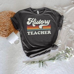 May include: A dark gray t-shirt with the text "History Teacher" in a retro font with colorful stripes behind the text.