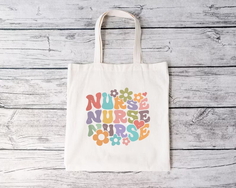 Puede incluir: Una bolsa de lona blanca con un dise&ntilde;o retro colorido que dice "NURSE" rodeada de flores y corazones.