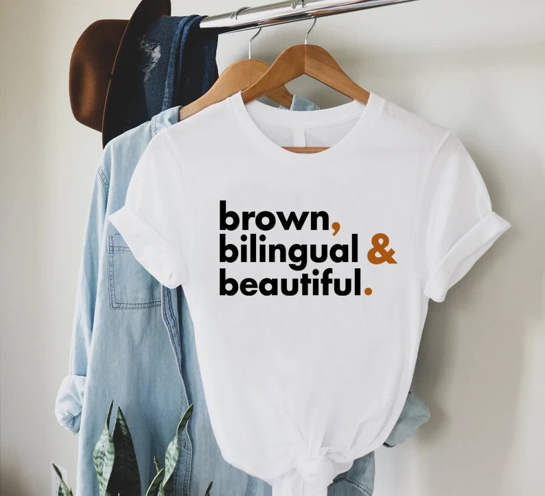 May include: White t-shirt with the text "brown, bilingual & beautiful." printed in black and brown.