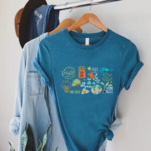 Puede incluir: Una camiseta azul turquesa con un estampado gr&aacute;fico de varios lemas e ilustraciones ambientales, incluyendo "Recicla", "Salva nuestros mares", "Piensa en verde", "No uses pl&aacute;stico", "M&aacute;s &aacute;rboles" y "Ahorra energ&iacute;a".