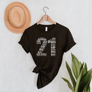 May include: Black t-shirt with a white graphic of the number 21 made up of words related to birthdays, such as "Happy", "Birthday", "Cake", "Friends", and "Gifts".