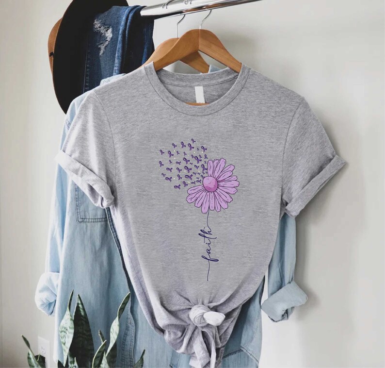 May include: Gray t-shirt with a purple flower design. The flower is made up of purple awareness ribbons and the word "faith" is written below it.