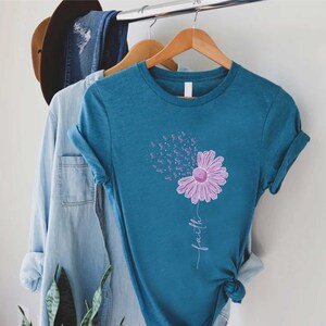 May include: Teal blue t-shirt with a purple flower design. The flower is made up of purple ribbon symbols and the word "faith" is written below the flower.